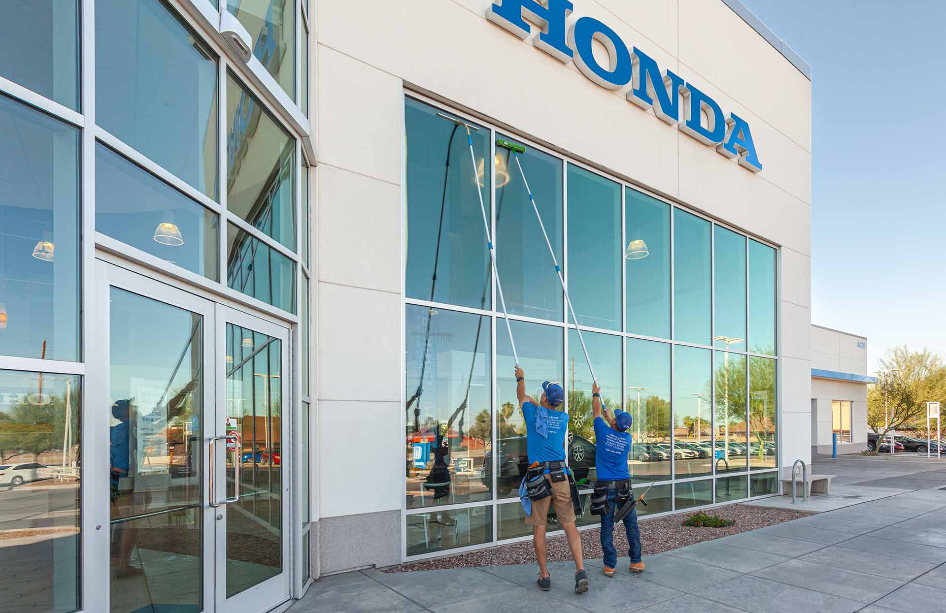 Two technician using poles to clean large exterior windows on a commercial building, representing professional storefront and office window cleaning.