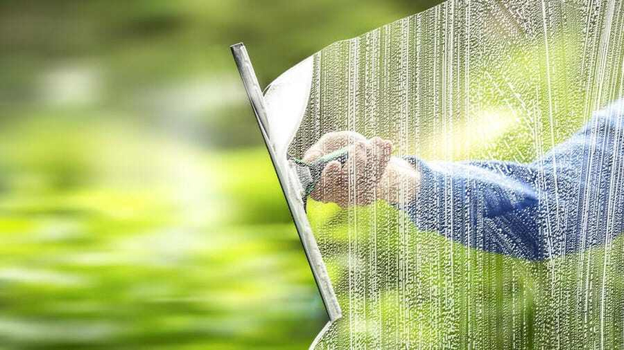 Close-up of a hand using a squeegee to clean a soapy window, representing professional residential window cleaning service.